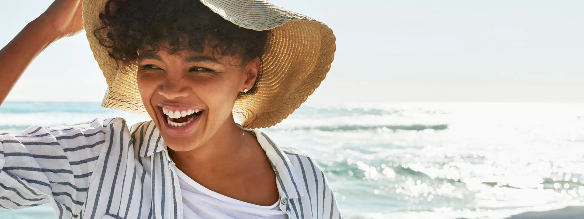 Woman at beach holding onto her hat